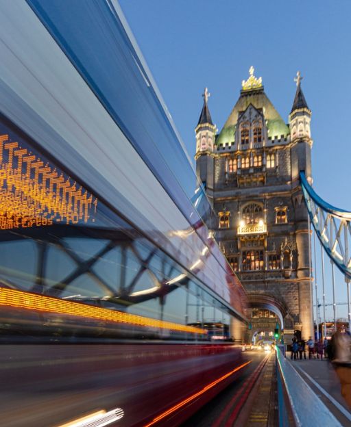 Tower Bridge at dusk with a red double-decker bus crossing, River Thames London