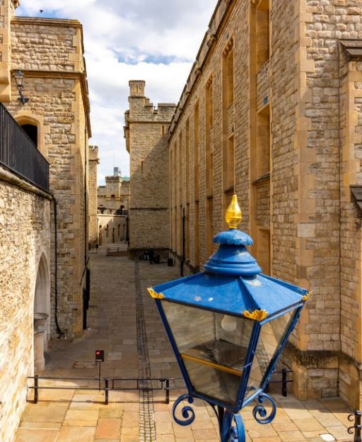 The inner courtyard of the Tower of London with a blue and gold gas lamp in the foreground and ancient stone walls beyond