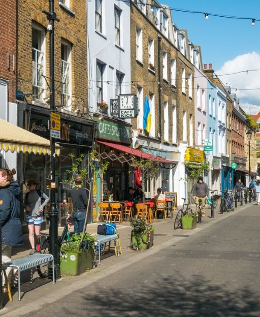 Exmouth Market street in Clerkenwell, London, lined with independent shops and outdoor cafe tables on a sunny day