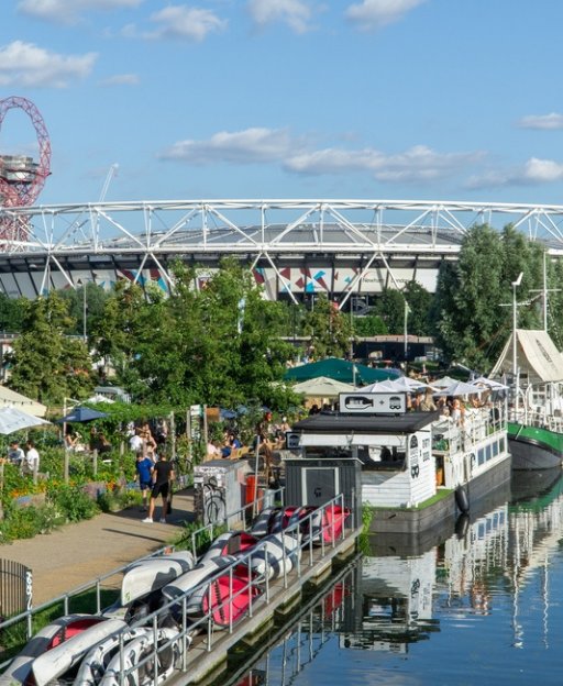 Canal-side view of Hackney Wick with boats moored along the waterway and the Queen Elizabeth Olympic Park in the background