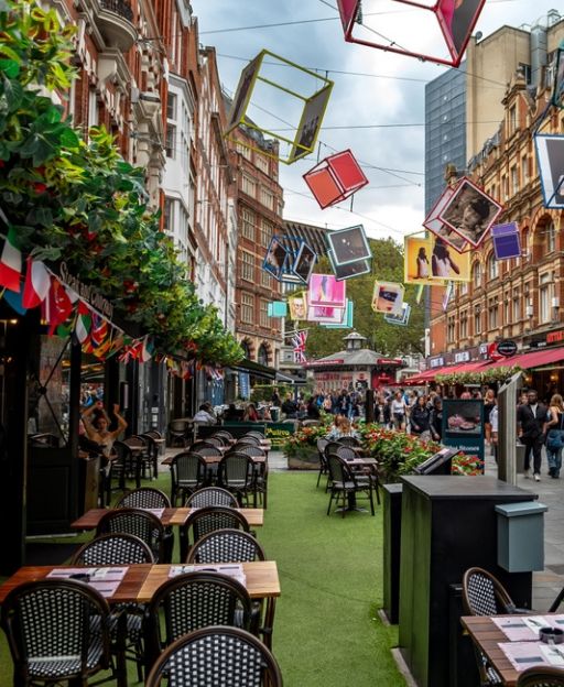 Outdoor dining in Covent Garden London with café tables colourful hanging art installations and Victorian architecture