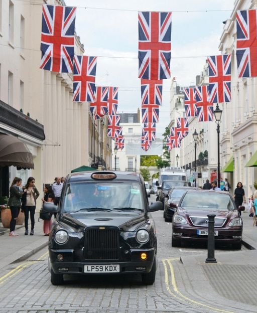 A black London taxi cab drives through a Mayfair street decorated with Union Jack bunting