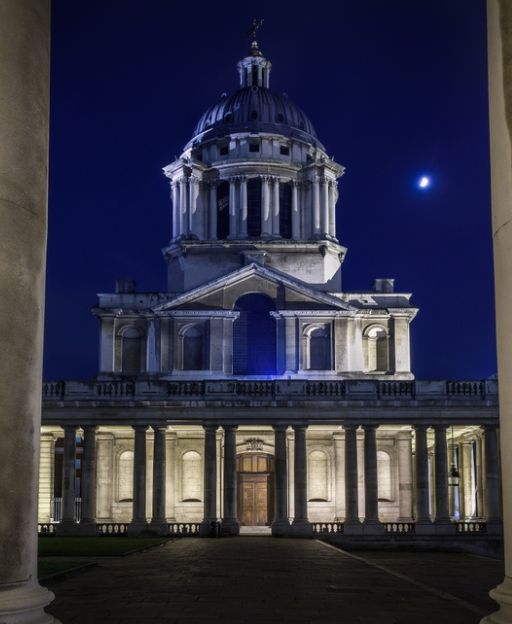 The Old Royal Naval College in Greenwich at night, its baroque dome illuminated against a deep blue sky