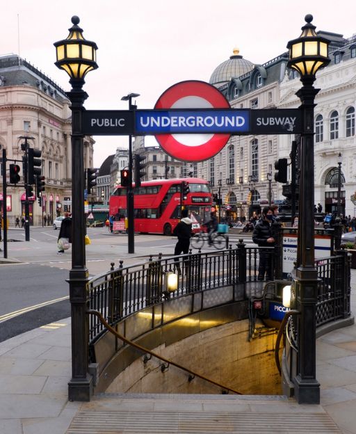 Piccadilly Circus Underground Station entrance with iconic London Underground sign and red double-decker bus in the background