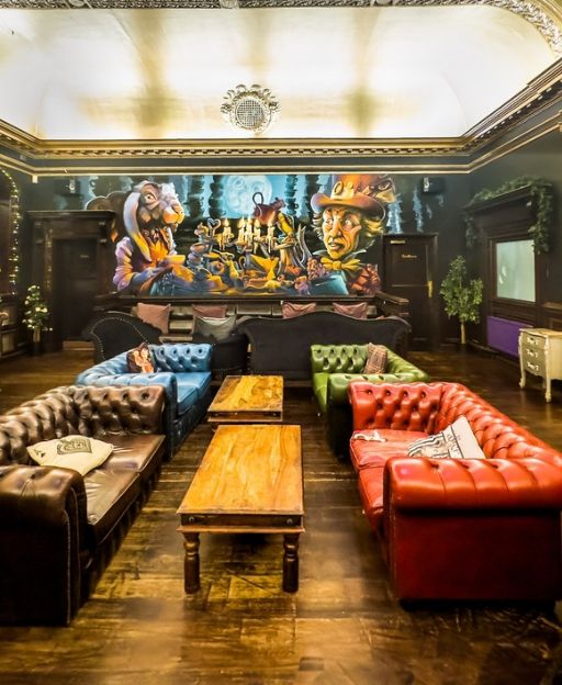 The Rabbit Hole pub interior in Streatham, South London, with colourful Chesterfield sofas and an Alice in Wonderland mural covering the wall