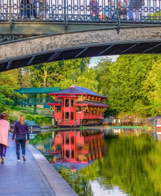 People walking along Regent's Canal towpath in London at golden hour, with a red floating restaurant reflected in the water