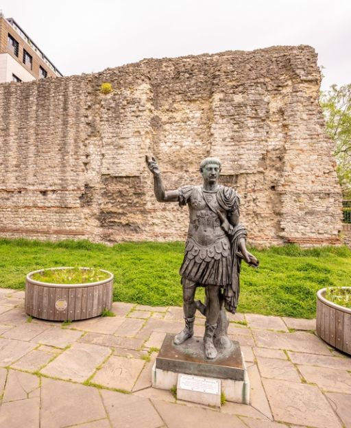 Emperor Trajan statue standing in front of the ancient Roman Wall in the City of London