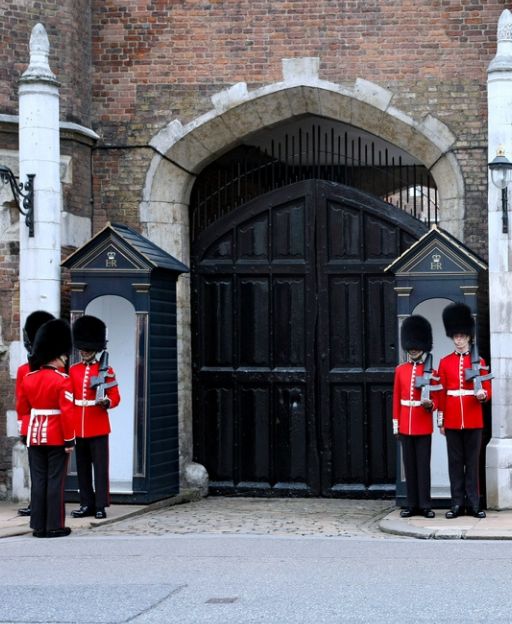 Royal Guards in scarlet uniforms and bearskin hats standing at St James's Palace gates in London