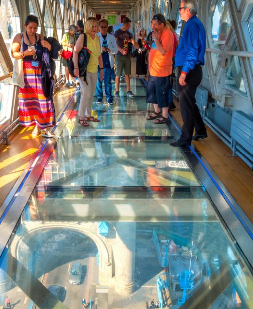 Tourists standing on the glass floor walkway of Tower Bridge, looking down at the Thames 42 metres below