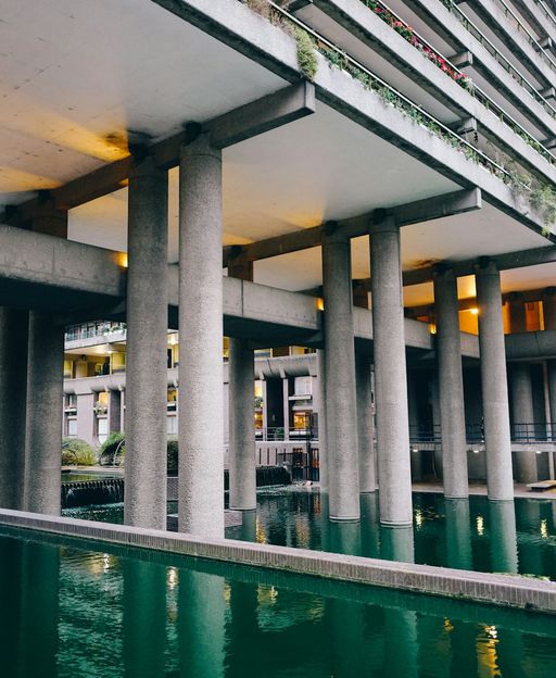 The Barbican Centre ornamental lake with concrete columns reflected in teal water, London