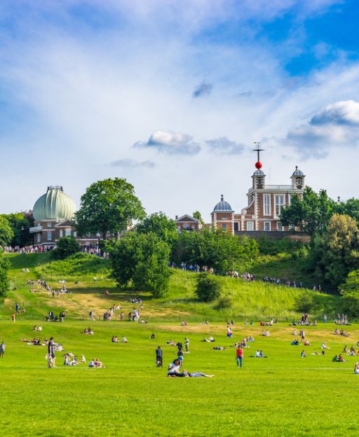 Greenwich Park on a sunny summer day with the Royal Observatory in the background and people relaxing on the grass