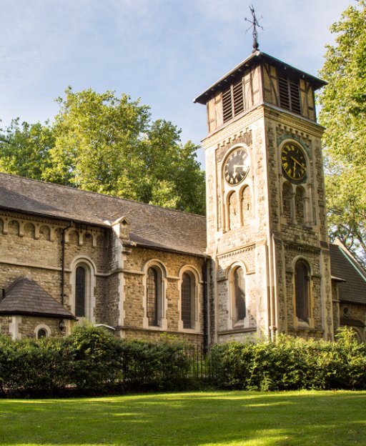 St Pancras Old Church stone tower with clock faces surrounded by trees in Camden, London