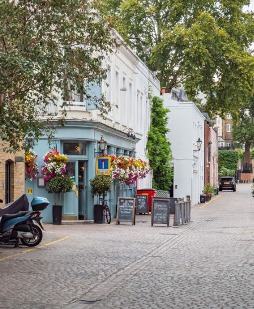 A cobblestone mews street in South Kensington, London, with a charming blue pub adorned with flower baskets