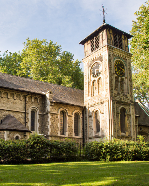 St Pancras Old Church exterior with clock tower and green trees