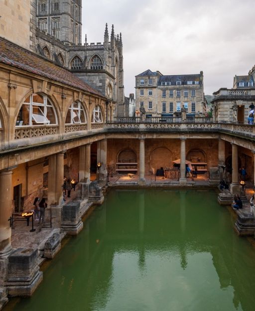The Roman Baths in Bath with steaming green water and Bath Abbey in the background