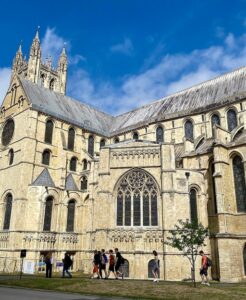 The exterior of Canterbury Cathedral in Kent, England, showing the Gothic towers and stonework on a sunny day with visitors in the foreground