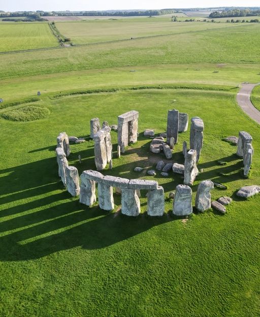 Aerial drone view of Stonehenge stone circle surrounded by green Wiltshire countryside on a sunny day