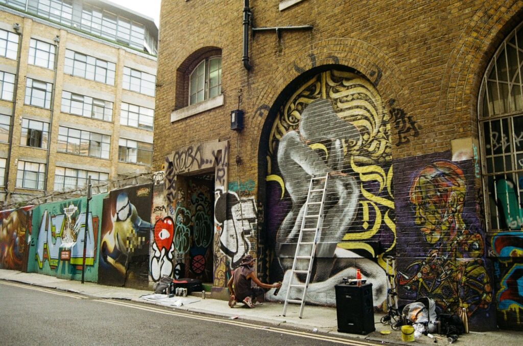Street art on a Brick Lane wall, with an artist at work.