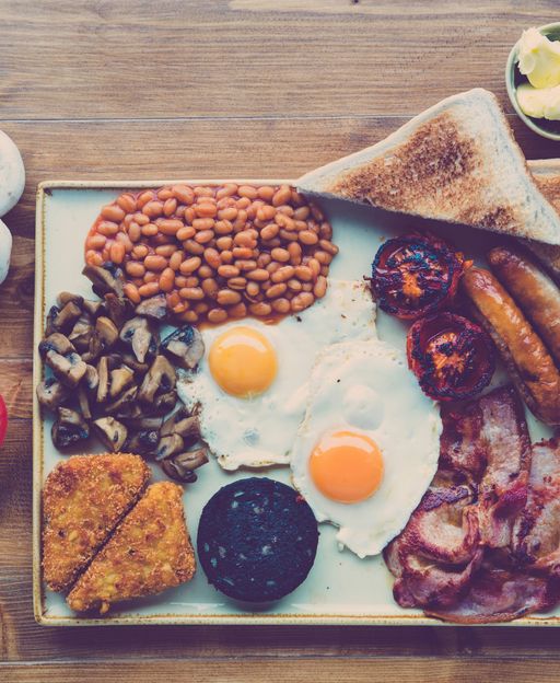 A classic full English breakfast with eggs, bacon, sausages, beans, tomato, and toast on a plate