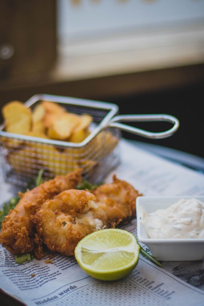 Fried fish and chips with tartare sauce and lime on newspaper.