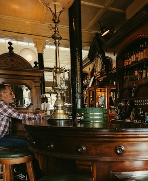 The ornate wooden bar of a traditional historic London pub, with brass fittings and period details