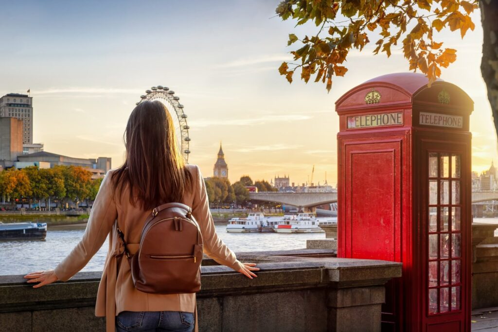 Woman by a red phone box looking over the Thames to the London Eye